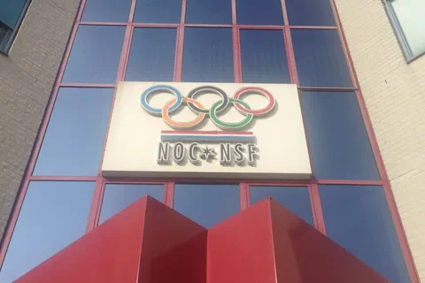Przeszklona fasada budynku z szyldem i kołami olimpijskimi holenderskiej organizacji NOC*NSF.