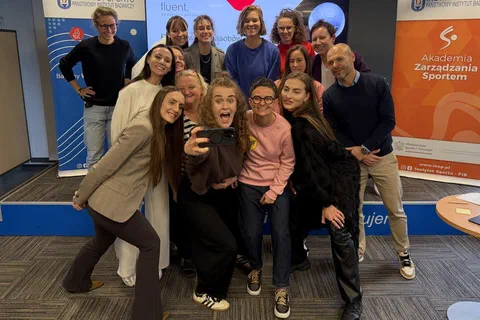 Uczestniczki i prowadzący robiący wspólne selfie w sali szkoleniowej.