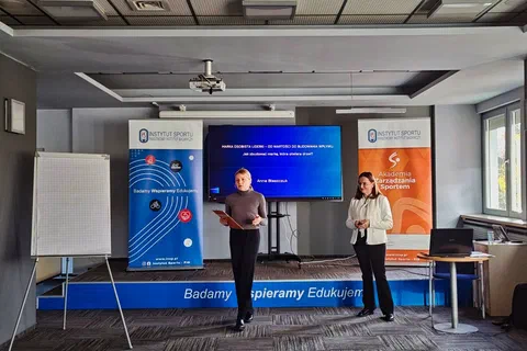 Dwie prowadzące stojące przed ekranem z prezentacją i roll-upami podczas otwarcia szkolenia w sali konferencyjnej
