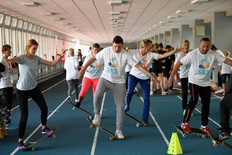 Uczestnicy zajęć praktycznych ćwiczący utrzymywanie równowagi na deskorolkach w hali sportowej