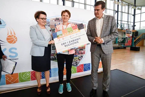 Wręczenie symbolicznego czeku z nagrodą na gry i zabawy ruchowe na tle ścianki SKS