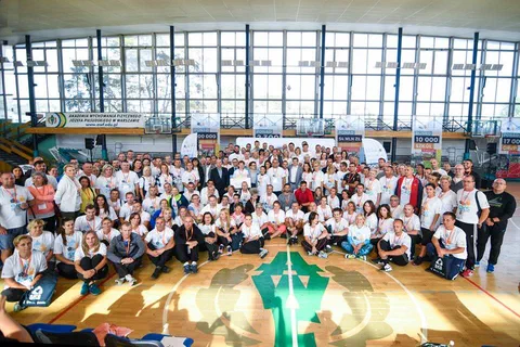 Duże zdjęcie grupowe uczestników konferencji w białych koszulkach na parkiecie hali sportowej AWF