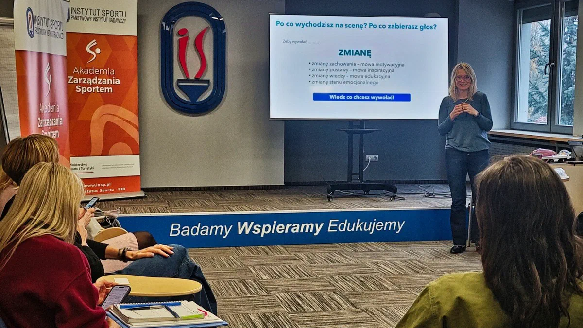 Prowadząca warsztaty wystąpień publicznych w sali szkoleniowej Instytutu Sportu – PIB przed ekranem z prezentacją „Co wychodzi na scenę? Po co zabierasz głos?”.