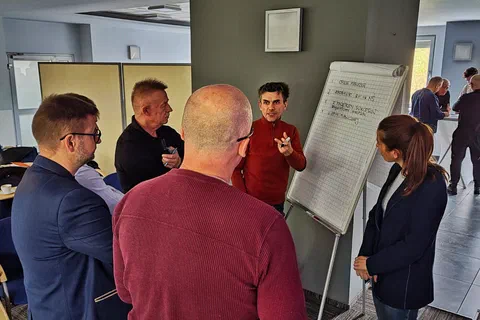 Pięcioosobowy zespół stojący wokół flipchartu i zapisujący wnioski podczas pracy w grupach