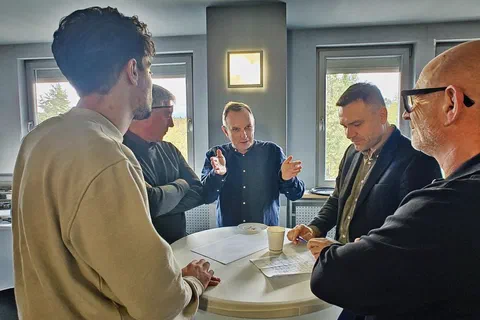 Czterech mężczyzn rozmawiających i robiących notatki przy okrągłym stoliku koktajlowym