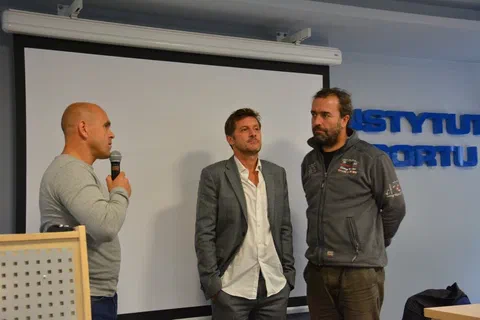 Trzech mężczyzn stojących przed ekranem projekcyjnym podczas sesji pytań i odpowiedzi z mikrofonem