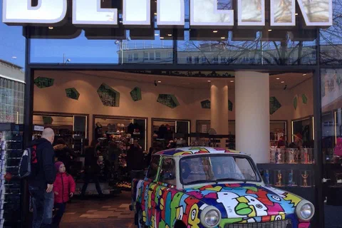 Kolorowo pomalowany samochód Trabant zaparkowany pod dużym podświetlanym napisem Berlin przed wejściem do budynku