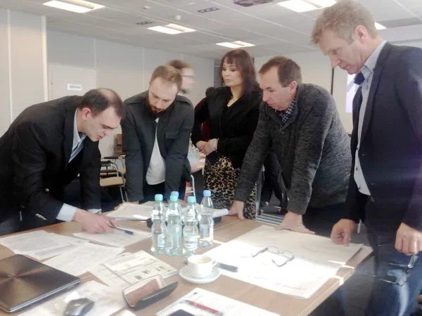 Uczestnicy spotkania roboczego analizujący dokumenty dotyczące standardów kwalifikacji rynkowych w sporcie przy stole konferencyjnym.