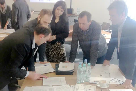 Pięcioosobowy zespół pochylony nad dokumentami i kartkami na stole podczas pracy warsztatowej