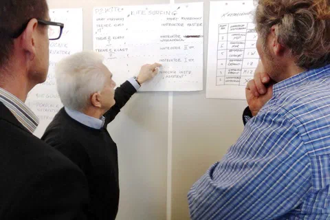 Trzech uczestników omawiających tabelę z efektami uczenia się zawieszoną na ścianie