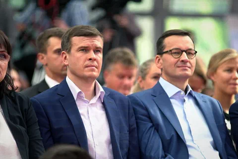 Goście oficjalni siedzący w pierwszym rzędzie na widowni podczas konferencji w hali sportowej