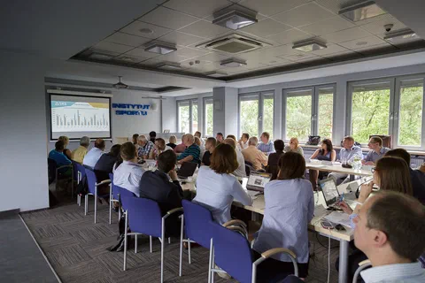 Widok ogólny sali konferencyjnej Instytutu Sportu z uczestnikami przy stołach i wykresem na ekranie