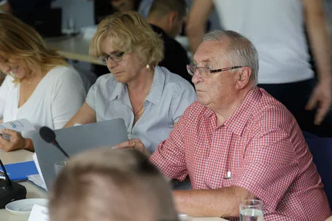 Trzy osoby przy stole konferencyjnym przeglądające dokumenty i ekran laptopa