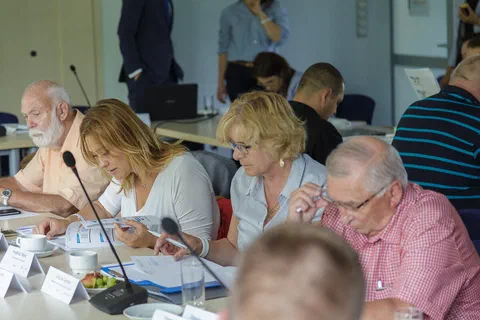 Cztery osoby siedzące w rzędzie przy stole konferencyjnym i analizujące wydrukowane materiały
