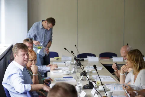 Mężczyzna nalewający wodę z butelki uczestnikom siedzącym przy stole konferencyjnym