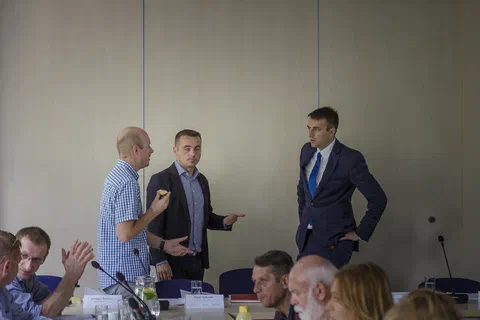 Trzej mężczyźni stojący z przodu sali i odpowiadający na pytania uczestników z sali