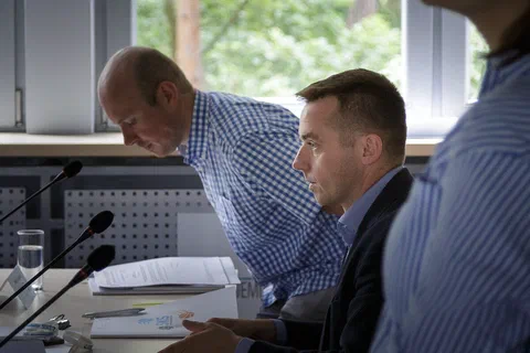 Mężczyzna pochylający się nad stołem podczas rozmowy z osobą siedzącą przy mikrofonie