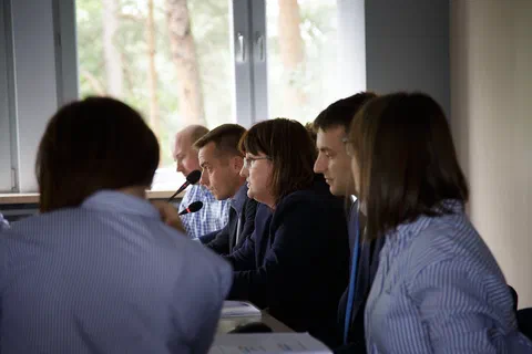 Grupa osób rozmawiających przy stole konferencyjnym na tle okna