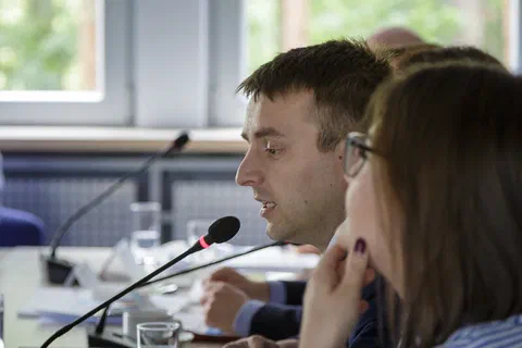 Pionowy kadr uczestników siedzących przy stole z mikrofonami i słuchających wystąpienia