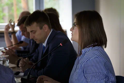 Zbliżenie na mężczyznę w garniturze i kobietę w okularach słuchających wypowiedzi przy stole