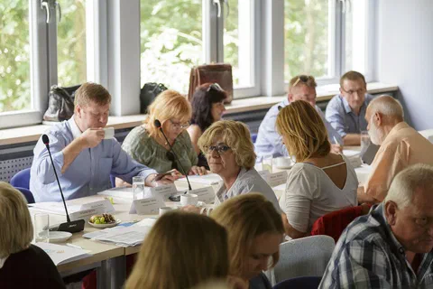 Grupa uczestników rozmawiająca przy stole konferencyjnym na tle okien