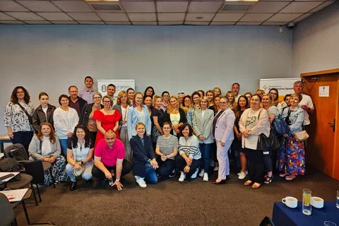Wspólne zdjęcie dużej grupy uczestników szkolenia ustawionych w dwóch rzędach w przestronnej sali