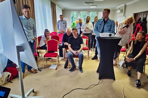 Dwaj uczestnicy omawiający notatki na flipcharcie przed grupą siedzącą w półkolu