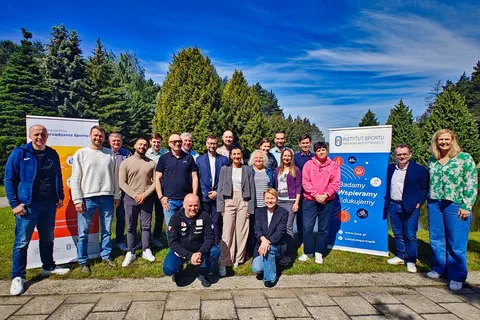 Zdjęcie grupowe uczestników szkolenia stojących na zewnątrz przed ścianą zieleni między dwoma roll-upami