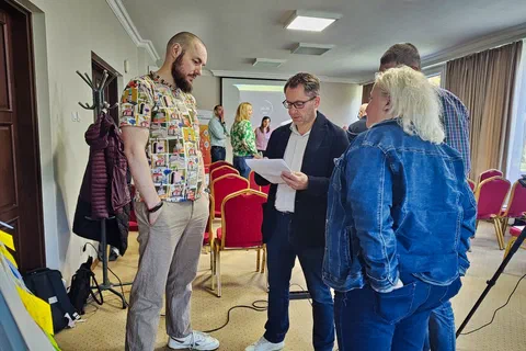 Trzy osoby dyskutujące nad kartką z notatkami podczas pracy warsztatowej w sali
