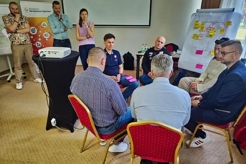 Czterech mężczyzn naradzających się w kręgu na krzesłach obok flipchartu z żółtymi karteczkami