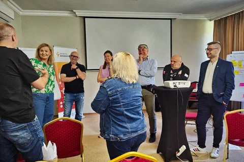 Sześcioosobowa grupa rozmawiająca na stojąco wokół stolika z projektorem podczas ćwiczenia