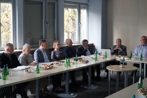 Uczestnicy posiedzenia siedzący przy stole konferencyjnym na tle okien podczas obrad