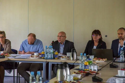 Pięć osób siedzących za stołem prezydialnym z mikrofonami i dokumentami podczas obrad