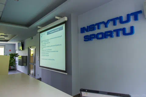 Ekran projekcyjny ze slajdem o podstawach prawnych działania obok napisu Instytut Sportu na ścianie