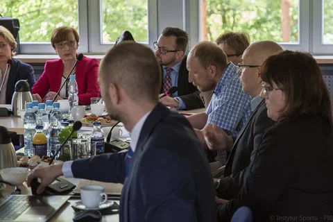 Zbliżenie na dyskusję członków prezydium i uczestników siedzących przy stole z mikrofonami