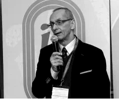 Czarno-białe zdjęcie prof. dr. hab. Zbigniewa Trzaskomy przemawiającego do mikrofonu na tle znaku Instytutu Sportu.