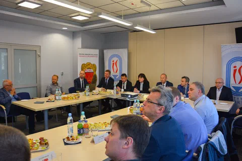 Szeroki kadr sali konferencyjnej z uczestnikami spotkania siedzącymi wokół stołu ustawionego w podkowę