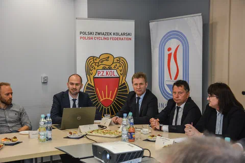 Czterech przedstawicieli siedzących przy stole na tle roll-upów Polskiego Związku Kolarskiego i Instytutu Sportu