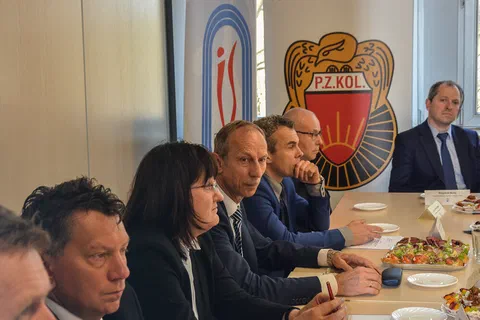 Pionowy kadr uczestników siedzących wzdłuż stołu konferencyjnego na tle banerów obu instytucji