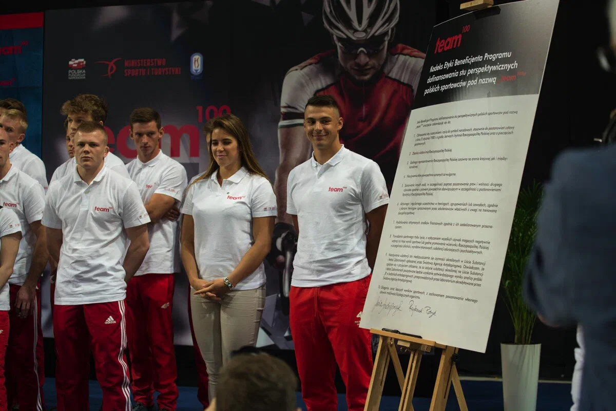 Zawodnicy programu Team100 na scenie podczas inauguracji programu przy planszy z zasadami programu.