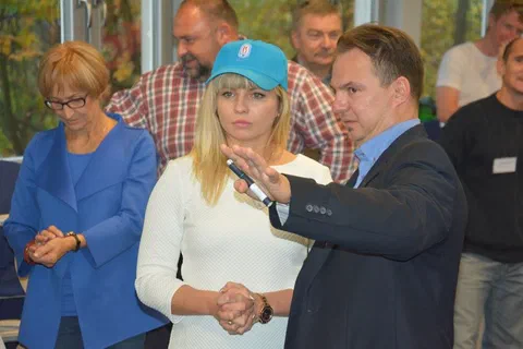 Prowadzący wręczający długopis uczestniczce w niebieskiej czapce podczas ćwiczenia grupowego