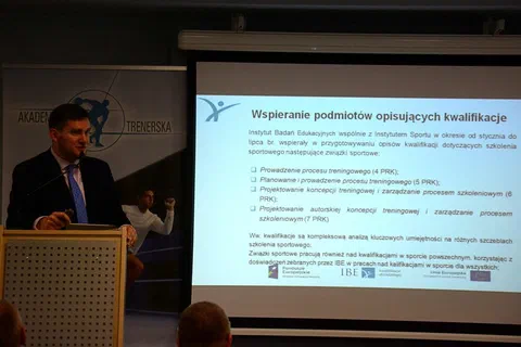 Wykładowca w garniturze prezentujący slajd o wspieraniu podmiotów opisujących kwalifikacje w sporcie
