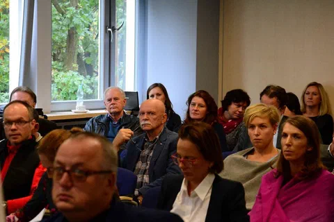Zbliżenie na grupę uczestników słuchających wystąpienia w sali konferencyjnej przy oknach