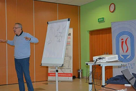 Prowadzący stojący obok flipchartu ze schematem i objaśniający zadanie warsztatowe