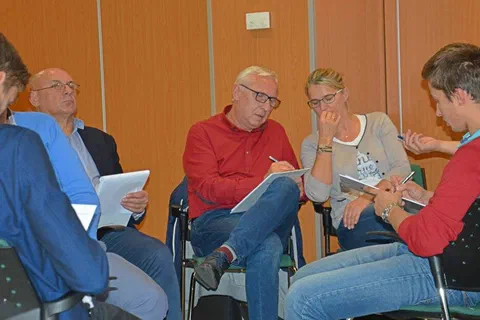 Czworo uczestników siedzących obok siebie i robiących notatki na podkładkach podczas pracy w grupie