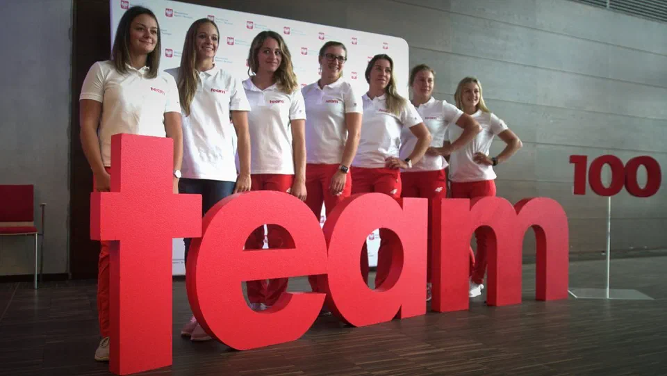Sześcioro zawodników programu Team100 stojących za przestrzennym napisem „team 100”