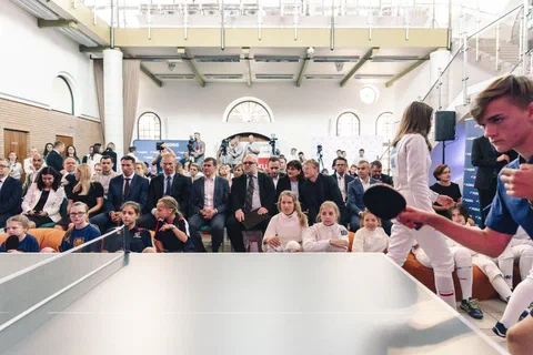 Młodzi zawodnicy grający pokazowo w tenisa stołowego przed zgromadzoną publicznością i gośćmi w pierwszym rzędzie