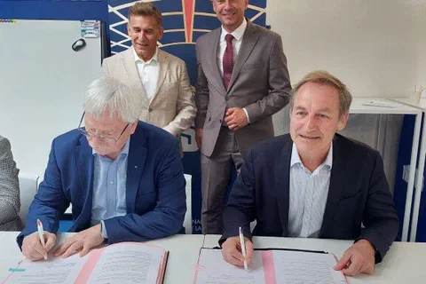 Dwaj dyrektorzy podpisujący przy stole porozumienie o współpracy w obecności dwóch stojących za nimi mężczyzn