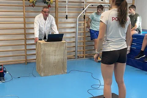 Zawodniczka stojąca z dłońmi na biodrach na platformie dynamometrycznej przed specjalistą z laptopem w sali gimnastycznej