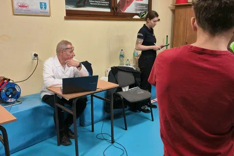 Specjalista przy laptopie rejestrujący wyniki pomiaru zawodnika stojącego na platformie badawczej